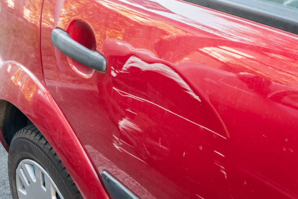 Red vehicle door with visible scratches and paint transfer before auto body repair service at Symtek Automotive.