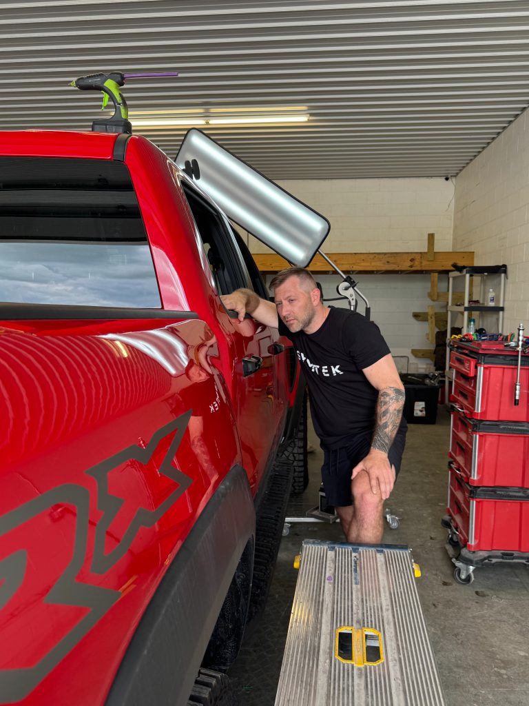 Symtek Automotive technician inspecting a red Jeep Rubicon with paintless dent repair lighting in Canton, Ohio.