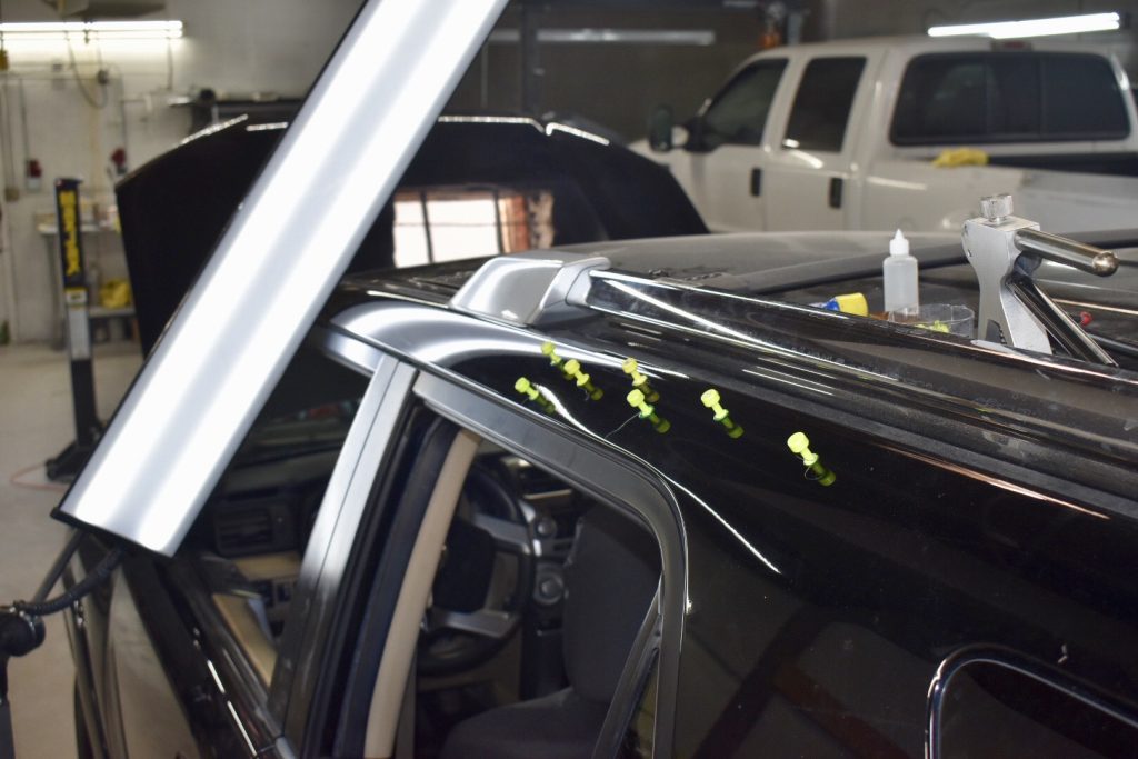 Black vehicle roof with glue tabs and repair lighting during paintless dent repair at Symtek Automotive in Canton, Ohio.